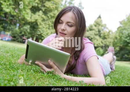 Frau mit Tablet-Computer liegt auf einer Wiese Stockfoto