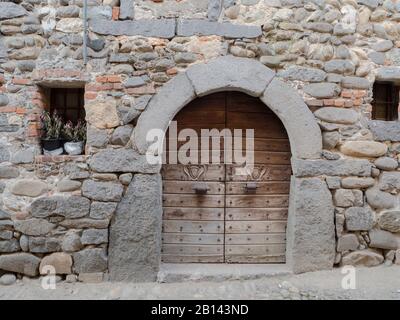 Ricetto di Candelo, mittelalterliche Holztür mit geschnitzten heraldischen Nieten und mit Steinen und Ziegelsteinen umrahmten Wappen.Piemont - Italien Stockfoto