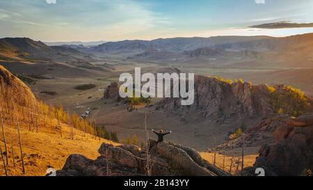 Mann sitzt auf Felsen mit ausgestreckten Armen, mongolische Schweiz, Wüste Gobi, Mongolei Stockfoto