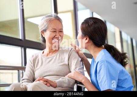 Freundliche Pflegekraft im Pflegeheim, die mit der asiatischen Seniorin im Flur spricht Stockfoto