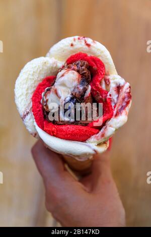 Frau, die ein rosenförmiges Eis mit Amarena, Schokolade und Erdbeeraroma hält, mit einer Kirsche oben in einem Zuckerkegel in Nizza, Frankreich Stockfoto