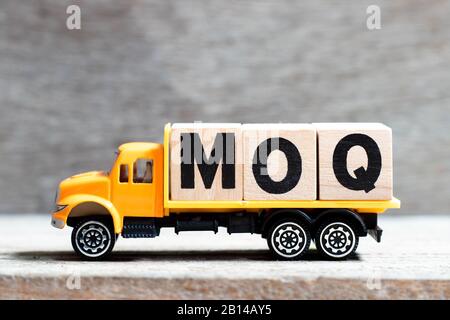 Fahrzeug hält Buchstabenblock in Wort MOQ (Abkürzung der Mindestbestellmenge) auf Holzhintergrund Stockfoto
