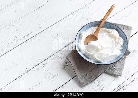 Hausgemachter griechischer Joghurt in Keramikschale auf weißem Holzhintergrund, Kopierraum. Frischer organischer einfacher Joghurt oder saure Sahne. Stockfoto