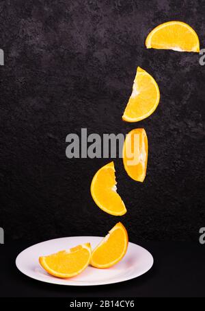 Orangefarbene Scheiben fliegen auf einem schwarzen Hintergrund in eine Platte. Fliegende Lebensmittel (orange). Kopierbereich. Stockfoto