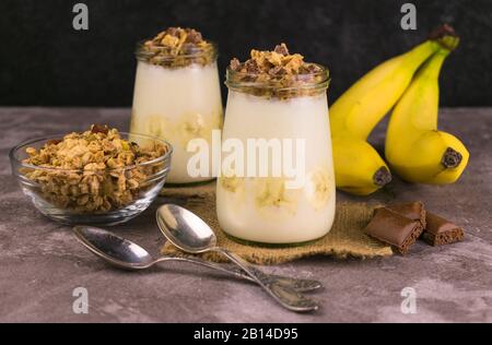 Weiches Dessert aus Bananenjoghurt und Granola auf dunklem Hintergrund. Nützliche Desserts. Stockfoto