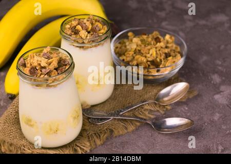 Weiches Dessert aus Bananenjoghurt und Granola auf dunklem Hintergrund. Nützliche Desserts. Stockfoto