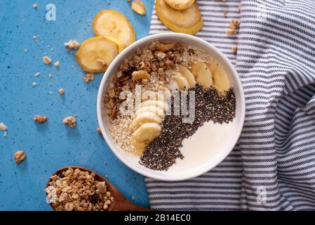 Smoothie-Schüssel mit Bananen, Chia, Sesam und Müsli auf blauem Grund Stockfoto