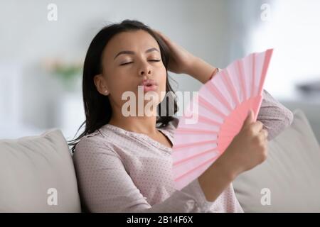 Ungesunde biraciale Frau atmet frische Luft vom Handfan Stockfoto