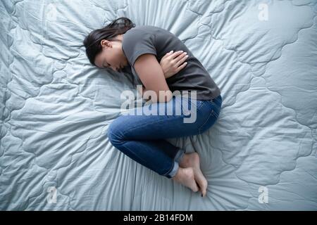 Ungesunde junge Frau, die im Bett liegt, fühlt sich depressiv an Stockfoto