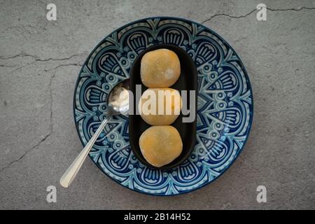 Gelb gefärbte japanische Mochi in Reisteig und auf einem blauen Plattenhintergrund. Traditionelles japanisches Dessert. Stockfoto