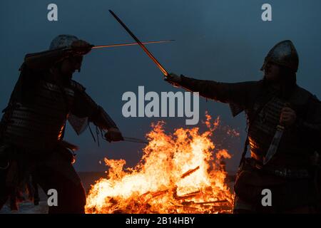 Reenactor im Kampf, während ein Langboot am Strand in Sheringham in Norfolk während des Sheringham Viking Festivals brennt, einer Feier des Norse Erbes der Küstenstadt. Stockfoto