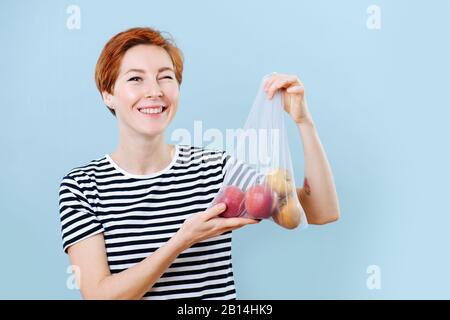 Winkende fröhliche Frau, die Äpfel in einer Netztasche zeigt Stockfoto