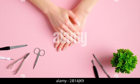 Frau bekommt professionelle Maniküre im Nagelsalon. Top View weibliche Hände und Maniküre Werkzeuge auf pinkfarbenem Hintergrund. Konzept für Schönheitsbehandlungen Stockfoto