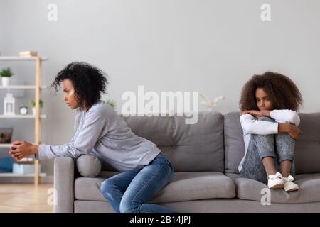 Genervte afrikanische alleinerziehende Mutter und aufrührende Tochter sitzen auf dem Sofa Stockfoto