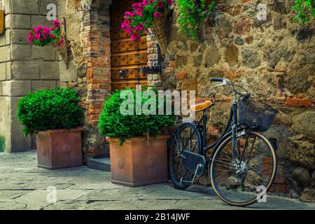 Altmodisches Retro-Fahrrad auf der Straße geparkt. Eingang und Holztür mit Blumen und Blumentöpfen, Pienza, Toskana, Italien, Europa Stockfoto