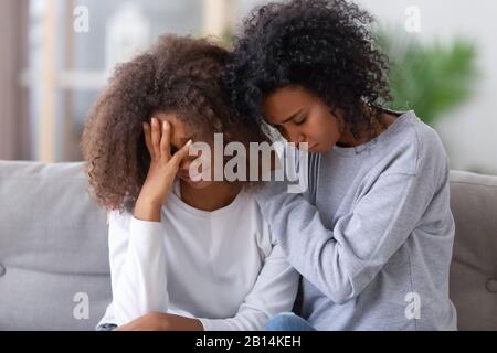 Aufgeregt afroamerikanische Mutter umarmte traurige Teenager-Mädchen mit Trostpflaster Stockfoto