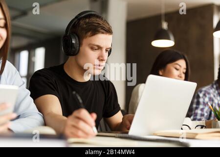 Bildungskonzept. Konzentrierter Kerl, der Hausaufgaben in der Bibliothek macht Stockfoto