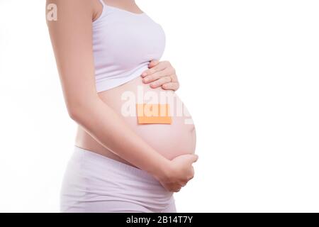 Schwangere Frau mit leerem Notizblock auf dem Bauch, anonymisiertes Gesicht. Schönes asiatisches weibliches Modell in ihren 20er Jahren. Schwangere Frau isoliert auf weißem Backgrot Stockfoto