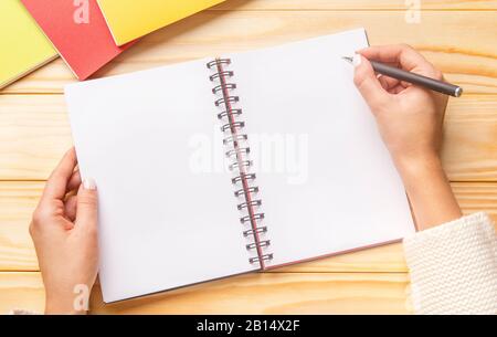 Weibliche Hände zeichnen sich in einem Spiralnotizbuch am Holztisch ab Stockfoto