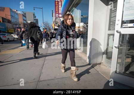 Eine Amerikanerin mittleren Alters spaziert auf der Main Street mit Tassen Starbucks-Kaffee. In Chinatown, Flushing, Queens, New York City. Stockfoto
