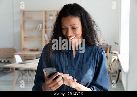 Fröhliche junge Frau aus der Vogelwelt, die Smartphone hält und auf den Bildschirm blickt. Stockfoto