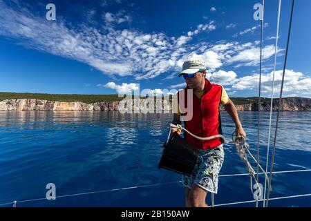 Ein Mann mit einem Eimer geht zum Deck der Yacht und wascht. Stockfoto