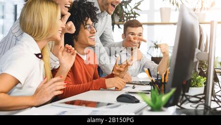 Fröhliches junges Team feiert professionellen Erfolg und schaut auf den Bildschirm des Laptops Stockfoto