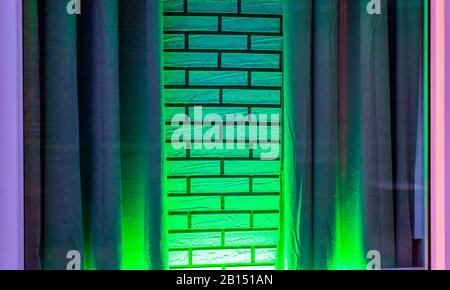Grünes Neonlicht, das auf einer weißen Ziegelwand mit Vorhängen und modernem dekorativem Hintergrund leuchtet Stockfoto