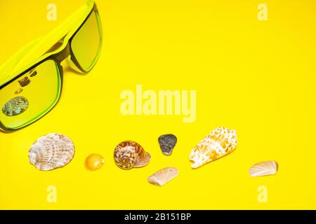 Sonnenbrille Meeresschalen leuchtend gelber Hintergrund. Konzept Sommerferien Reisen. Draufsicht Stockfoto