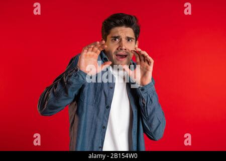 Erschrockene europäer fürchten sich vor etwas und blicken mit großen Augen voller Horror über roten Wandhintergrund in die Kamera. Stockfoto