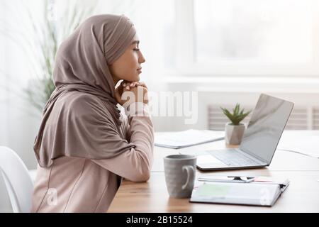 Porträt einer nachdenklichen arabischen Unternehmerin, die am Arbeitsplatz im Büro sitzt Stockfoto