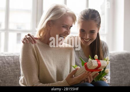 Überglücklich aufgeregte neugierige Frau mittleren Alters, die auf ein unerwartetes Geschenk blickt. Stockfoto