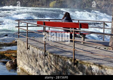 Frau auf einer roten Bank genießt den Blick auf den Rheinfall bei Schaffhausen Stockfoto