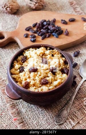 Süßer Hirseporridge mit dunklen Rosinen in einer rustikalen Keramikschale Stockfoto