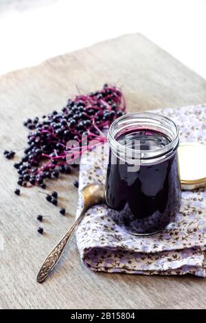 Hausgemachter schwarzer Elderberry-Sirup in Glasbecher und bunte schwarze Elderbeere im Hintergrund, Kopierraum Stockfoto