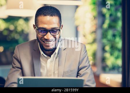 Lächelnder Afro-Typ in Brille, der im Büro Musik hört Stockfoto