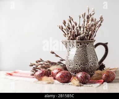 Osterstillleben mit Pysanka und Weidenzweigen in Keramikkanne auf traditionellem ukrainischem Tuch. Dekorierte Ostereier, traditionell für Eastern Europa Stockfoto