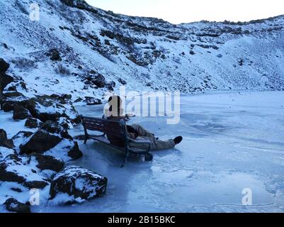 Ein Kerl sitzt auf einer Bank, die in Lake Kerid im Krater eines erloschenen Vuklan gefroren ist. Wunder von Island im Winter. Stockfoto