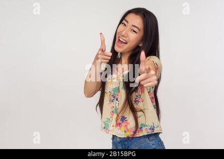 Hey, glücklicher Gewinner! Begeisterte asiatische Mädchen in der Sommer-Bluse, die mit Fingerpistolen auf die Kamera zeigt und Champion wählt, emotional reagiert Stockfoto