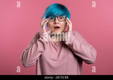 Nahaufnahme des jungen verängstigte Mädchens mit blauem Haarstyling, das isoliert über dem rosafarbenen Hintergrund schreit. Gestresste und depressive Frau Stockfoto