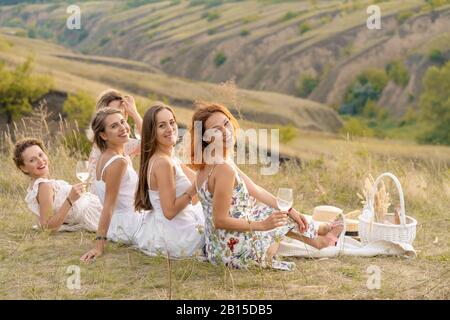 Die Firma fröhliche weibliche Freunde in weißen Kleidern mit Blick auf die grünen Hügel, entspannen Sie bei einem Picknick Stockfoto