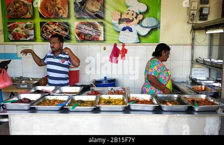 Ein Mann und eine Frau verkaufen indische Küche an einem Straßenrand. Auf der Theke Metalltabletts mit verschiedenen Schalen. Stockfoto