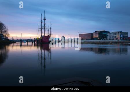 Lange Exposition der Überseestadt in Bremen, Deutschland mit Bürogebäude, Segelboot und perfekter Reflexion an der weser während der blauen Stunde, zuletzt Stockfoto