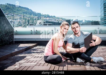 Jungen Erwachsenen persönlichen Fitness-Trainer (Coach) zeigt Ergebnisse und Erfolge, seine jungen weiblichen Kunden auf auf dem Dach des Gebäudes im städtischen Zentrum. Stockfoto