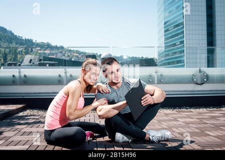 Jungen Erwachsenen persönlichen Fitness-Trainer (Coach) zeigt Ergebnisse und Erfolge, seine jungen weiblichen Kunden auf auf dem Dach des Gebäudes im städtischen Zentrum. Stockfoto