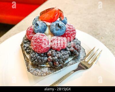Frischkäse-Beerenteppich auf einem weißen Teller mit Gabel. Frischkäse in Kunstschale, garniert mit Beeren. Stockfoto