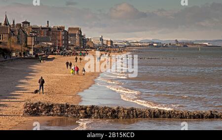 Portobello, Edinburgh, Schottland, Großbritannien. Februar 2020. Sonniger Nachmittag mit möglichen Windböen von 46 kmh, die den Sand am Strand aufschlagen, aber nach einer Woche starken Regens und winterlichen Schauern wurden Familien und Hundegänger dazu ermutigt, aus- und herauszukommen und das Beste aus den hellen Bedingungen zu machen. Auf den Hügeln im Hintergrund ist Schnee zu sehen. Credit: Arch White/Alamy Live News. Stockfoto