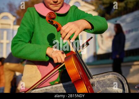Nahaufnahme Portrait Frau in grüner Jacke bereitet auf der Straße eine Geige zum Musizieren vor. Auftritt des Straßenmusikers Geiger Stockfoto