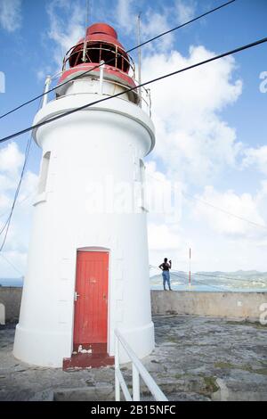 Der Leuchtturm steht majestätisch an einem hellen Tag und lässt eine Fotografin minusartig erscheinen Stockfoto