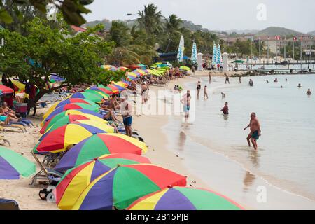 Viel touristische Aktivität und bunte Sonnenschirme, Spaß am Strand an einem beliebten Strand an einem hellen sonnigen Tag Stockfoto